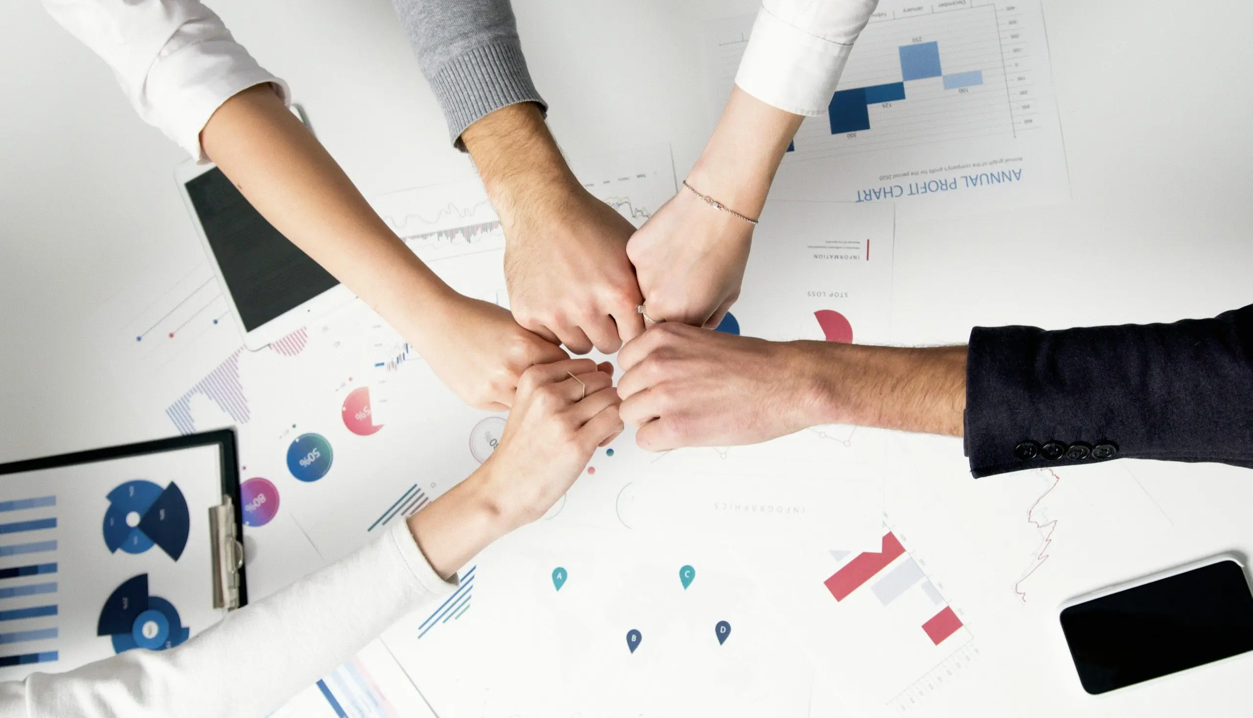 Cinq mains se rejoignant en un geste de solidarité au-dessus de documents et graphiques professionnels sur une table.