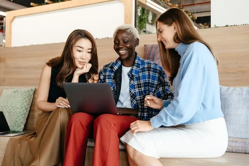 Trois personnes souriantes, regardent un ordinateur portable dans un environnement de travail collaboratif.”