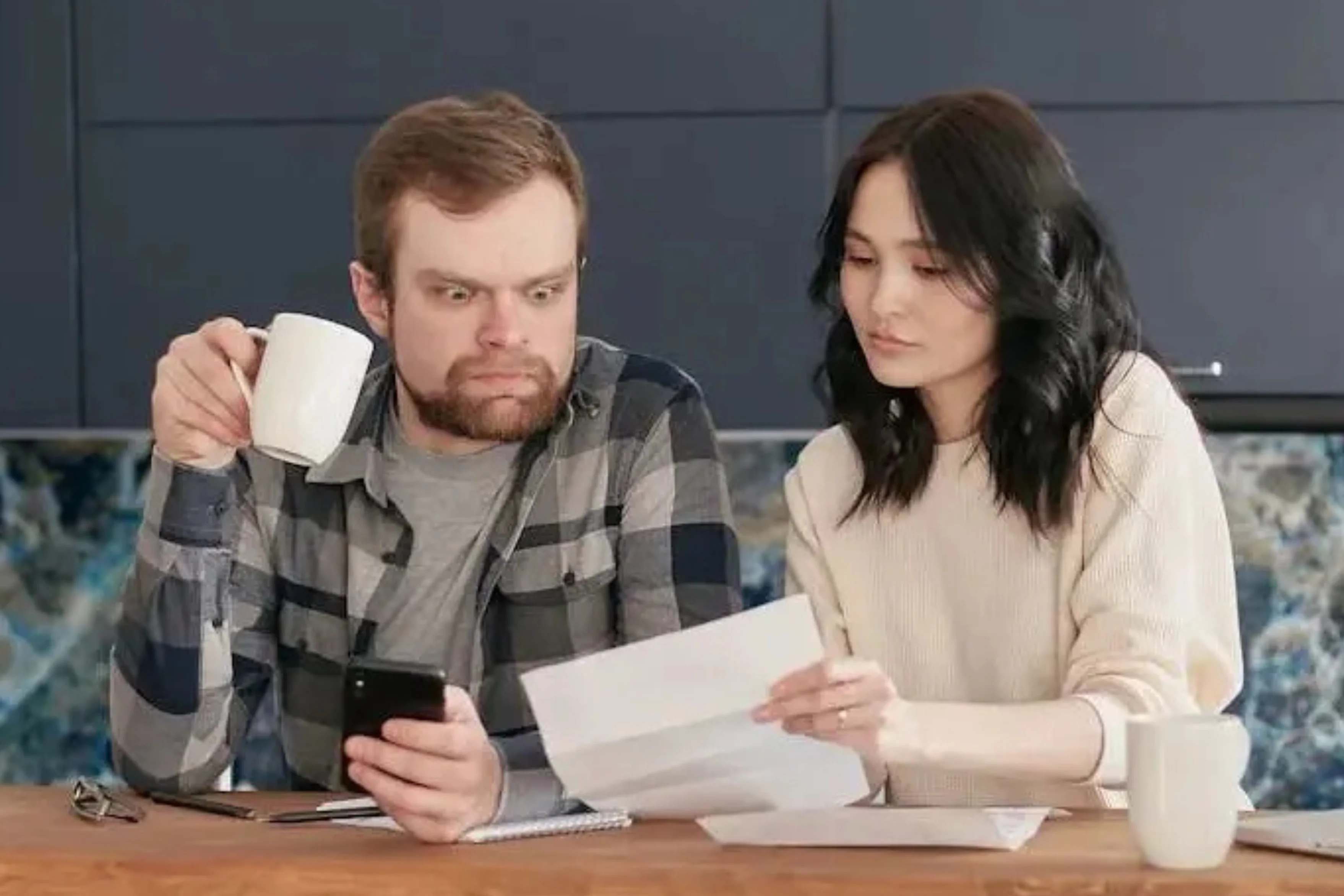 Un homme et une femme assis à une table, examinant des documents ensemble avec des tasses de café à côté.